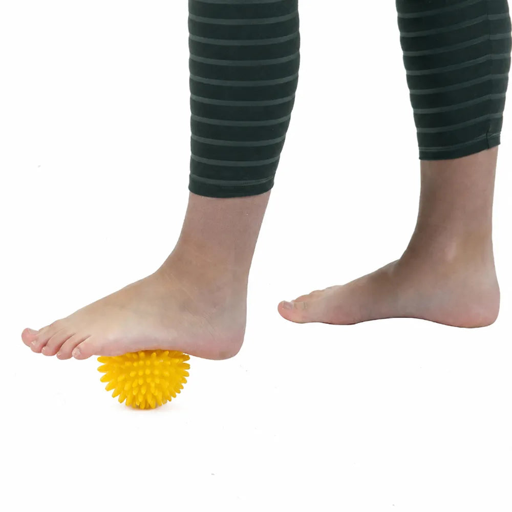 Massage de la voûte plantaire avec une petite balle sensorielle jaune de 8 cm à picots.