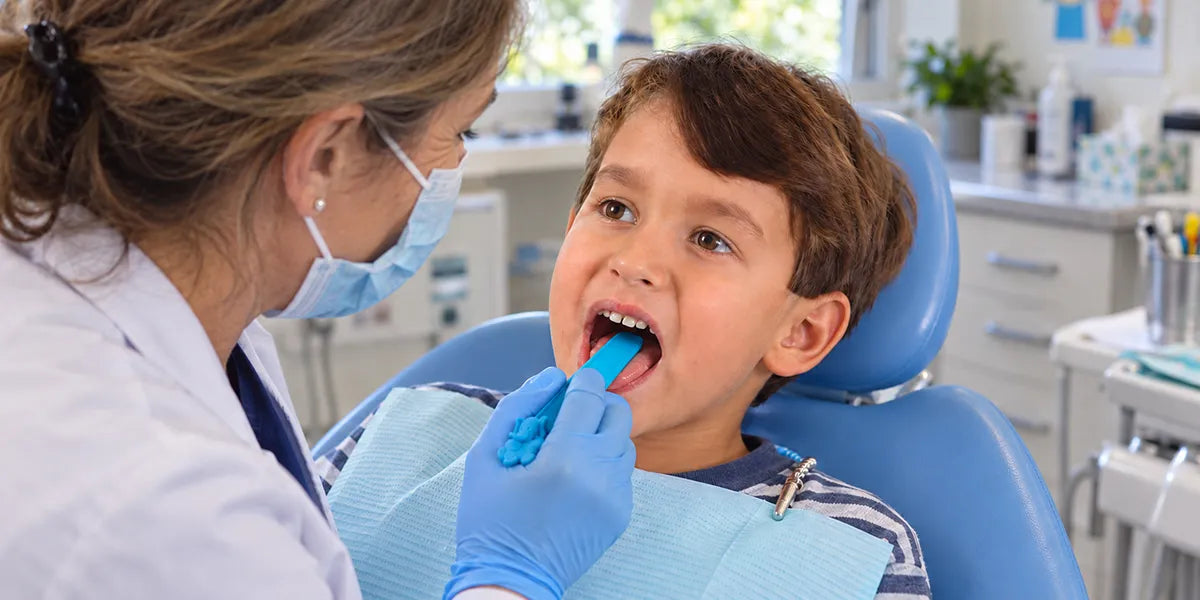 Dentiste utilisant un abaisse-langue aromatisé junior lors de l’examen bucco-dentaire d’un enfant