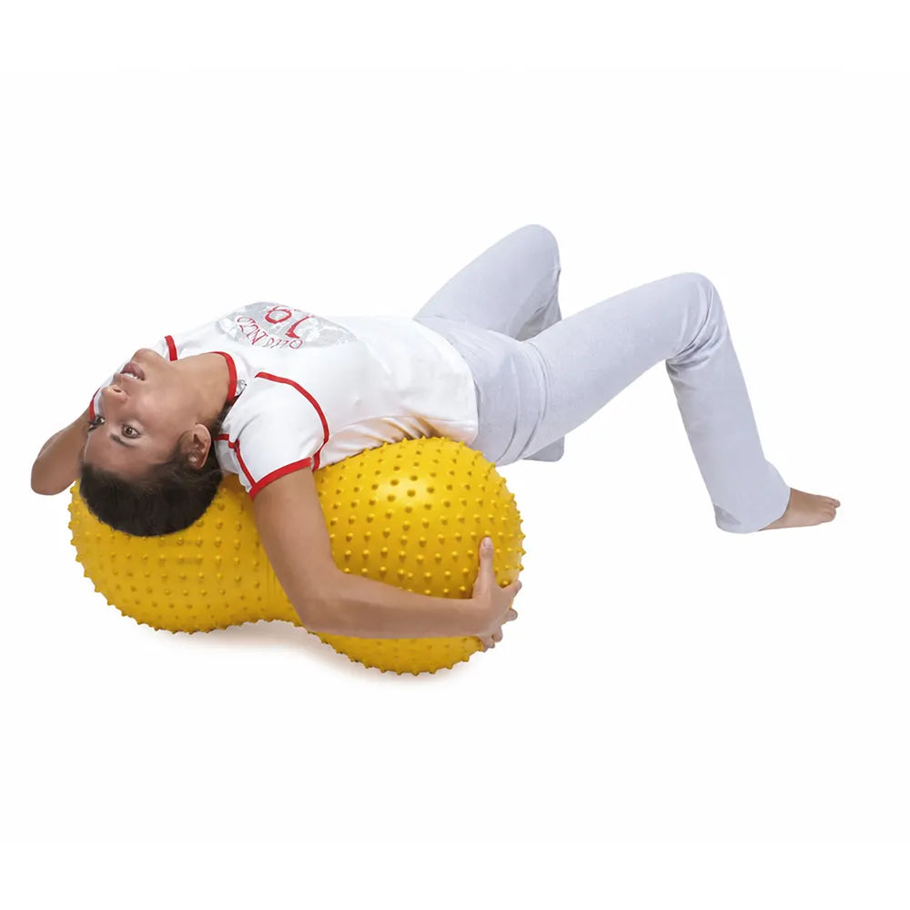 Femme allongée sur un ballon sensoriel jaune à picots en forme de cacahuète.
