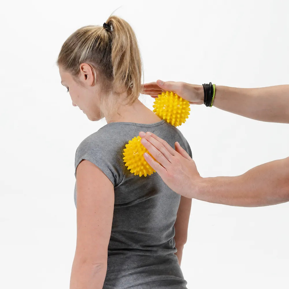 Massage du haut du dos et de la nuque avec deux petites balles sensorielles jaunes à picots.