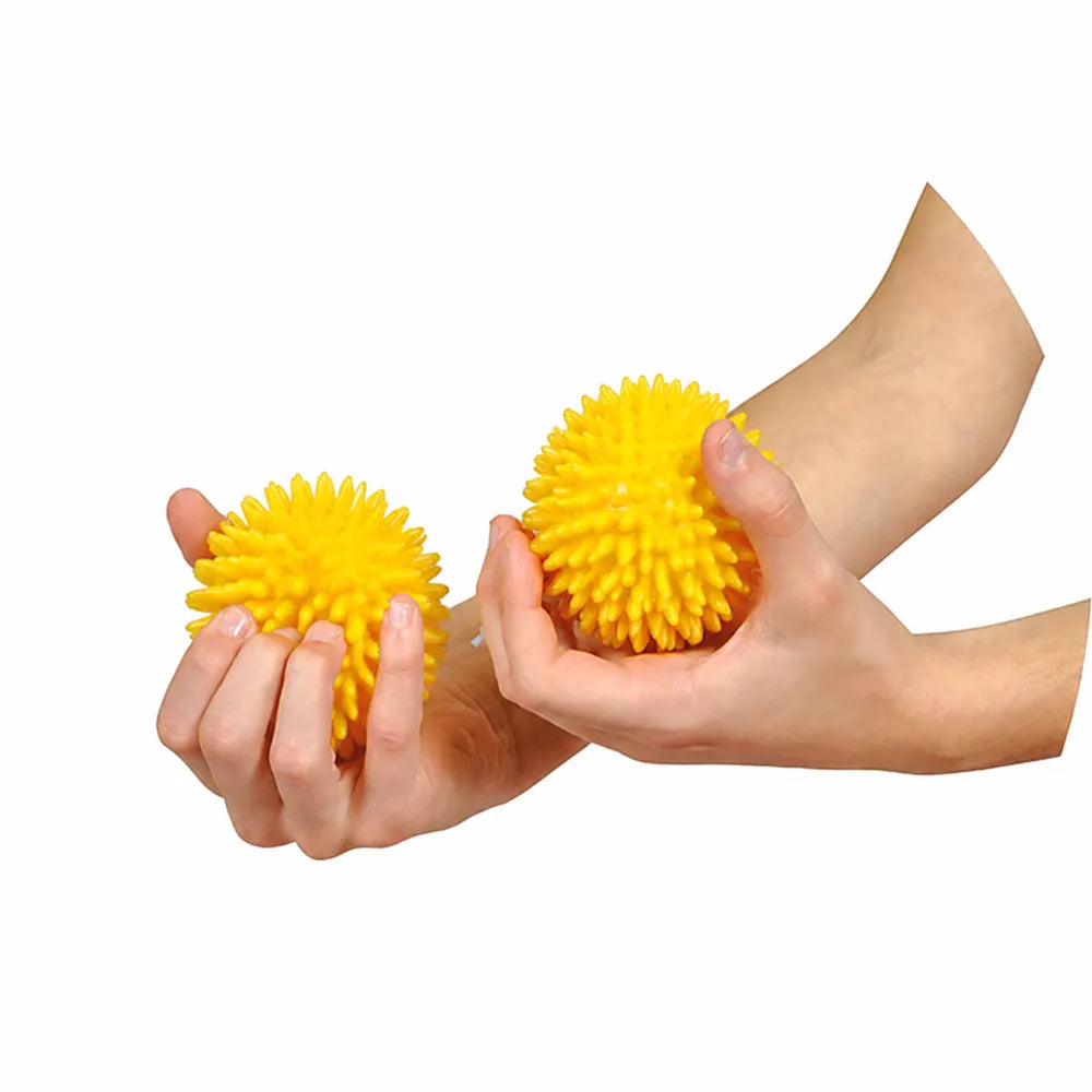 Deux petites balles sensorielles jaunes de 8 cm à picots tenues dans les mains.