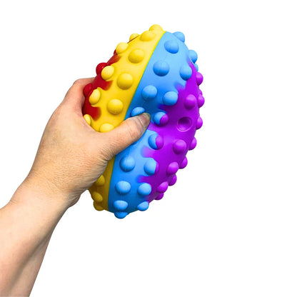 Main appuyant sur une bulle de la balle de rugby Pop It multicolore