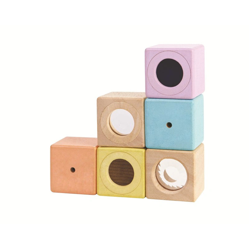 Blocs sensoriels en bois coloré avec effets visuels et sonores, empilés sur fond blanc